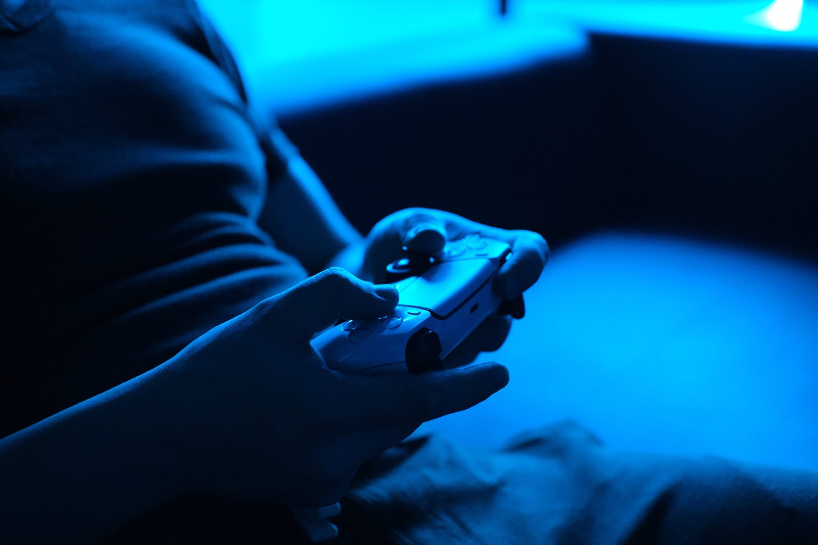 Young male gamer playing video game at home in the dark room using game console controller watching at LED TV. Gaming and entertainment concepts. Close up game console in hands